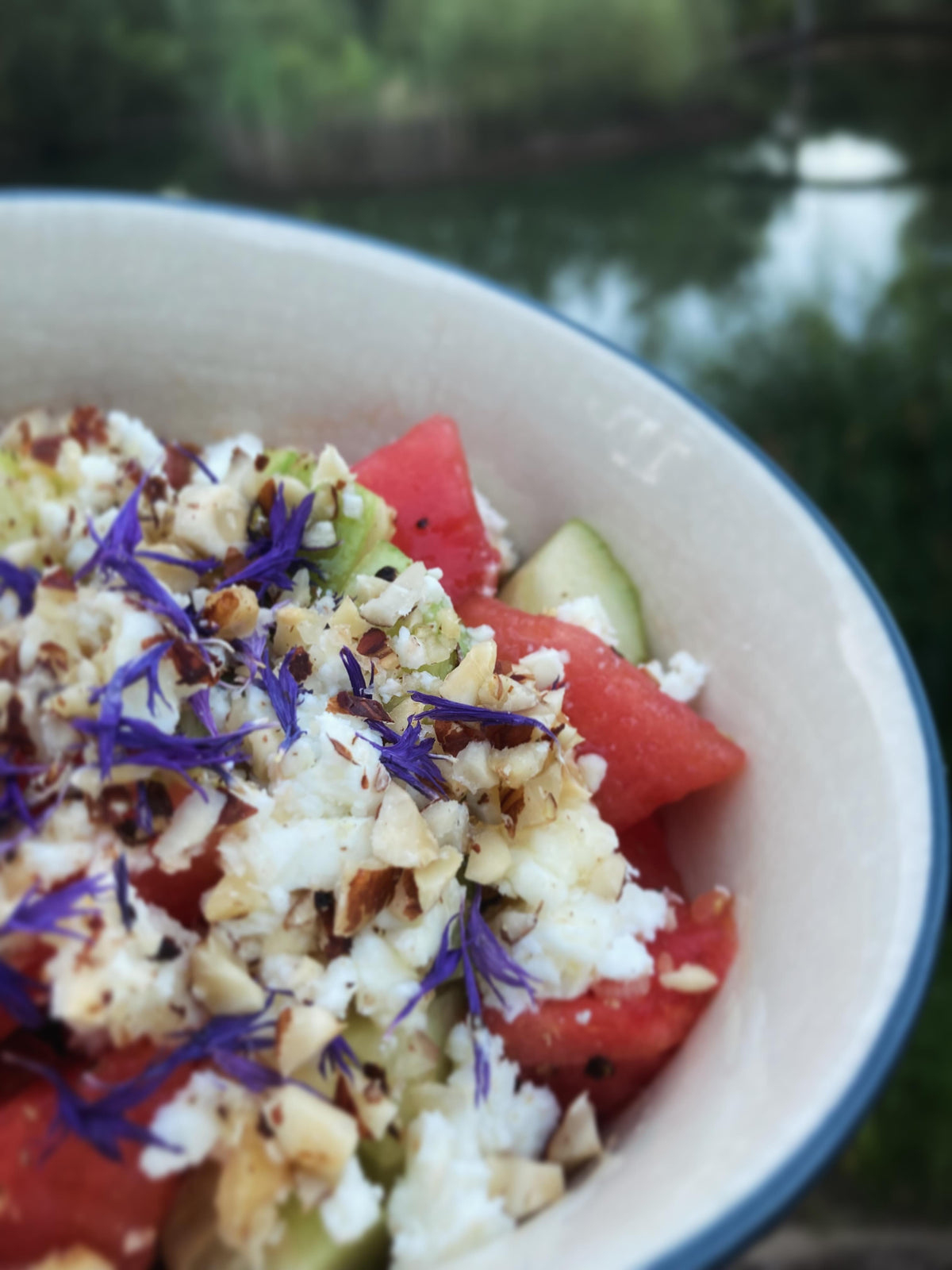 idée recette : une salade de pastèque et féta dans un bol, vue de près, sur laquelle on a parsemé quelques pétales de Bleuet mauve.